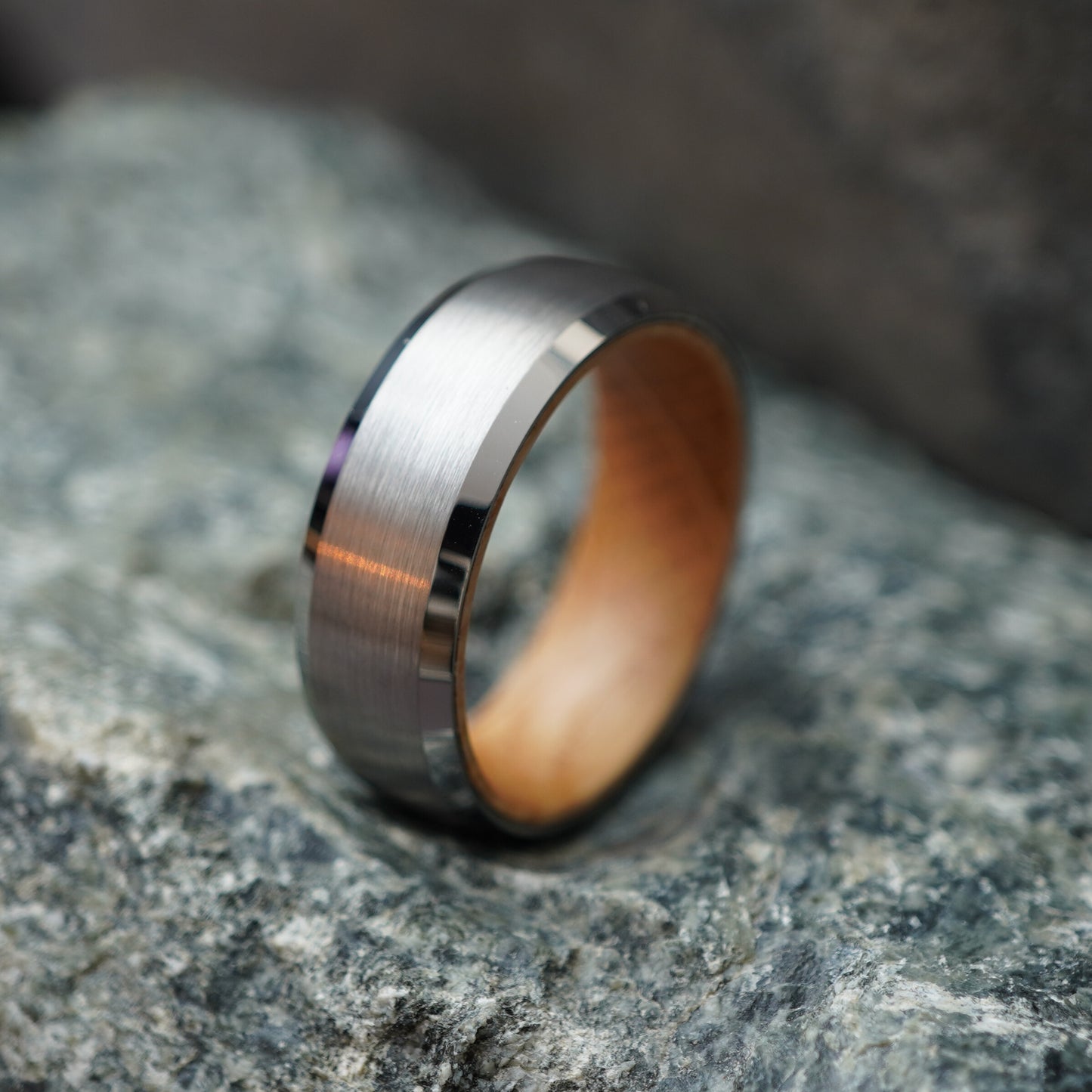 8mm men's ring by Forge and Lumber with brushed silver exterior and barrel wood interior, set on a rocky background.