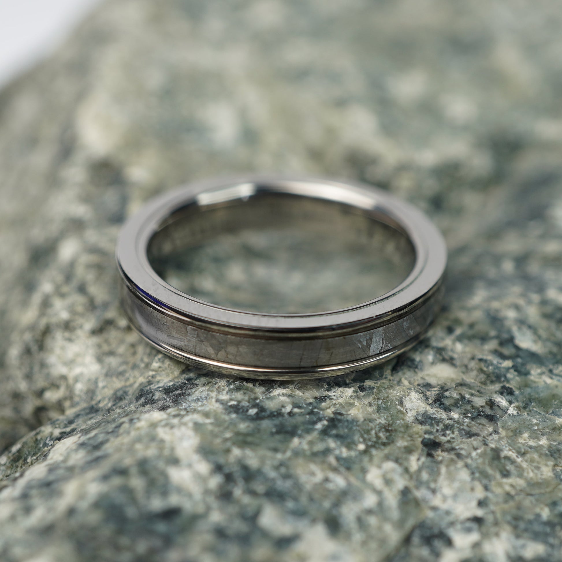 Silver ring with a polished finish and a gray inlay on a textured stone background.