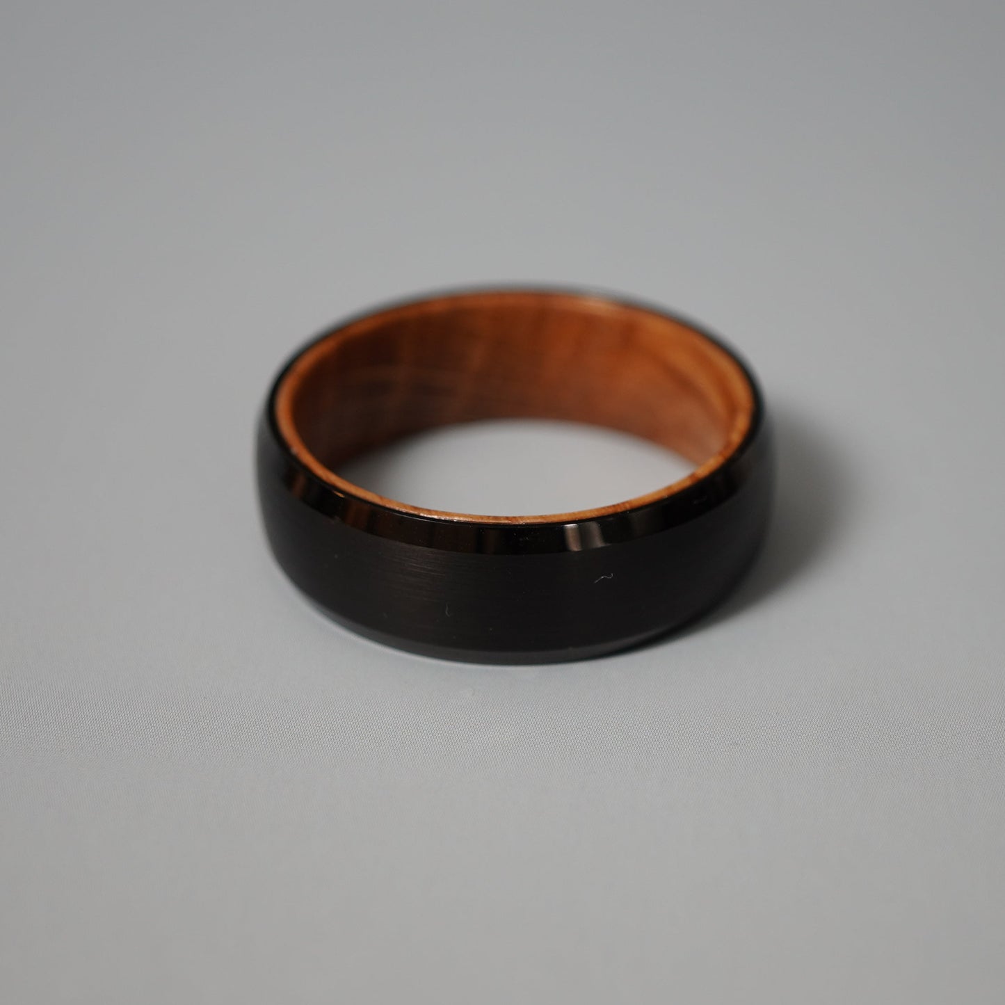 Black beveled-edge ring made from barrel wood by Forge and Lumber, showcasing a sleek design and natural wood interior.