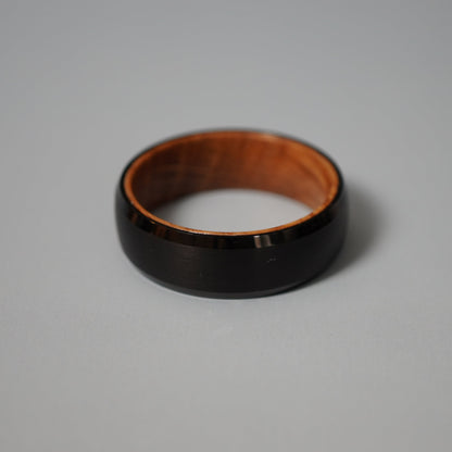Black beveled-edge ring made from barrel wood by Forge and Lumber, showcasing a sleek design and natural wood interior.