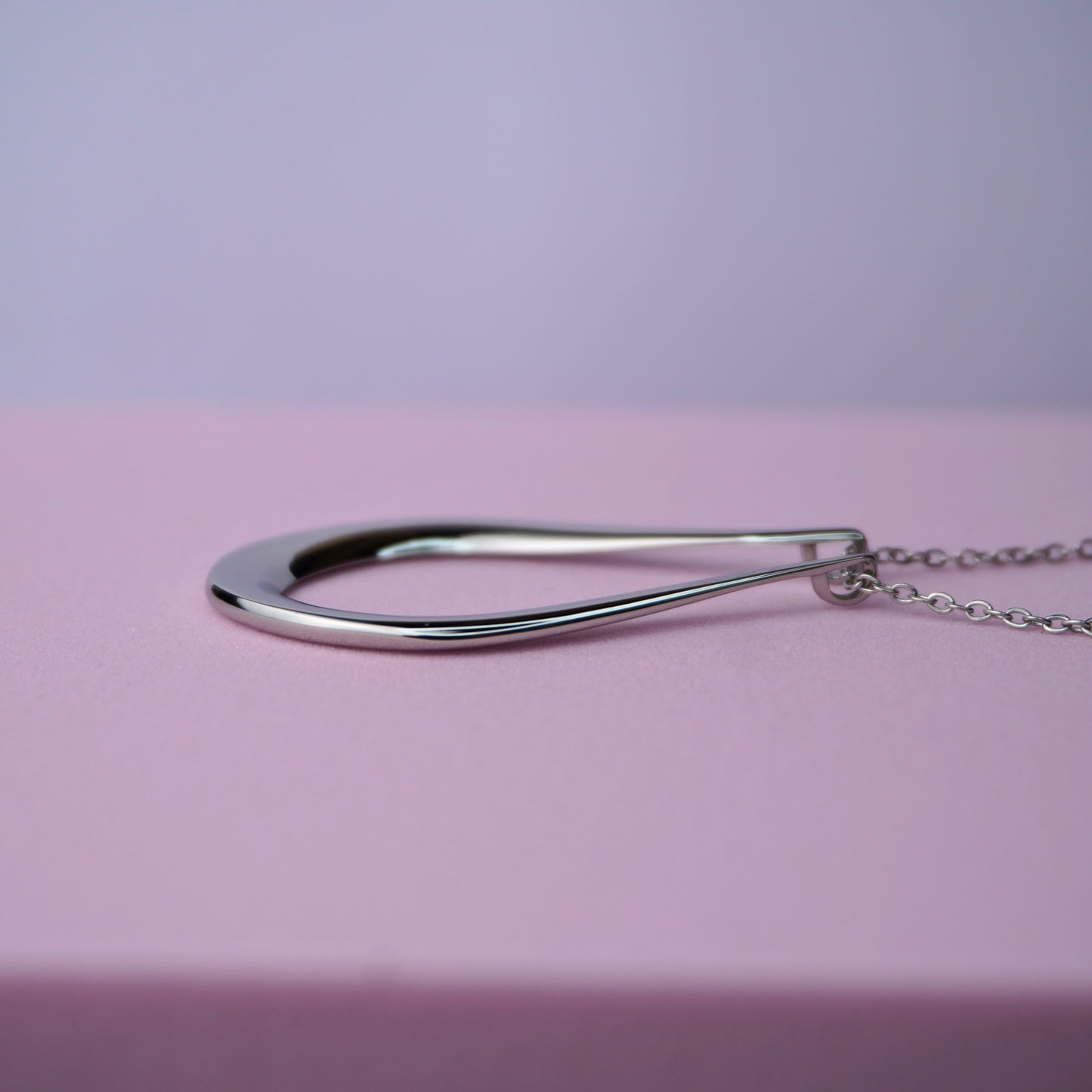 Silver teardrop pendant necklace on a delicate chain against a pink background.