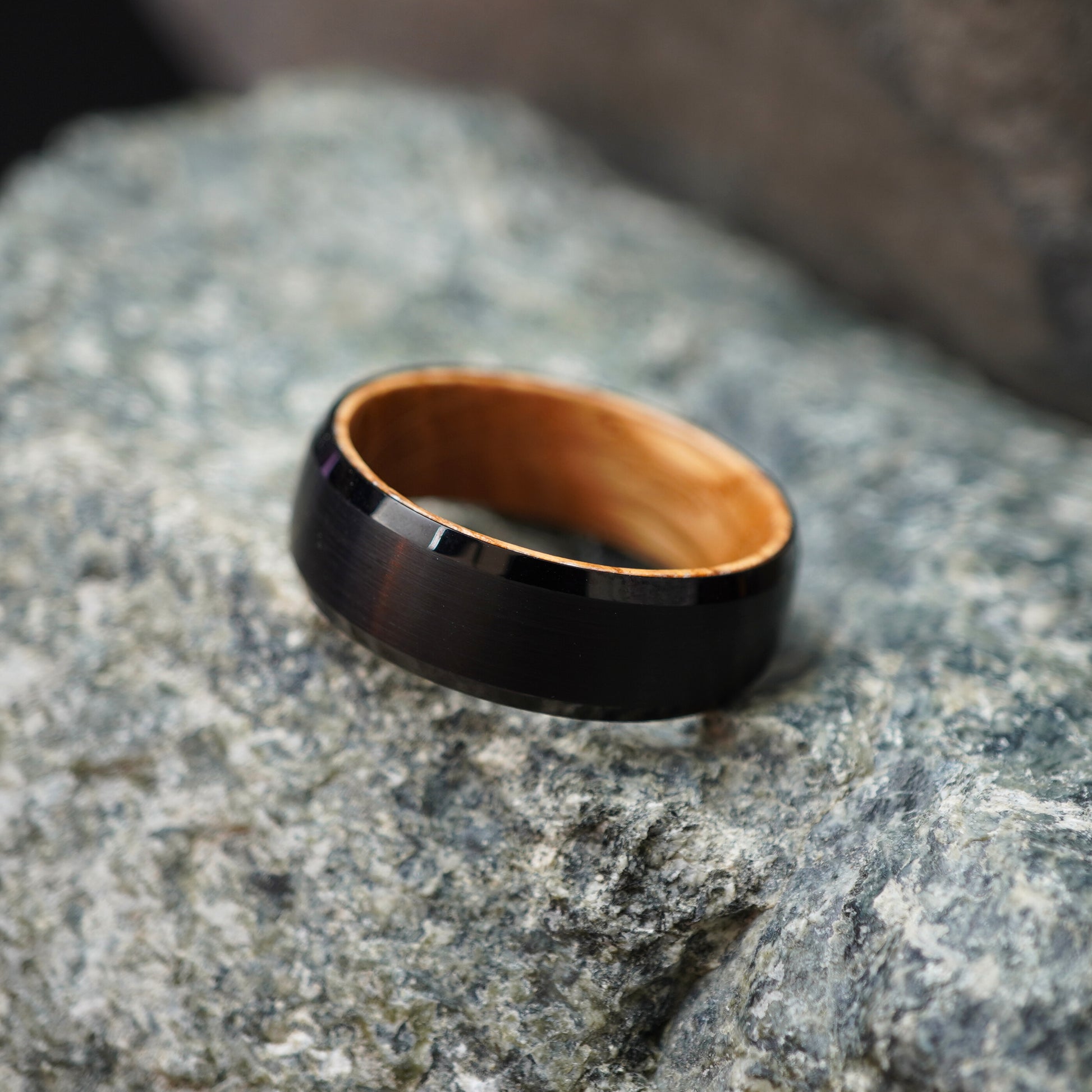 Black beveled-edge ring made from barrel wood by Forge and Lumber, showcasing a polished exterior and natural wood interior.