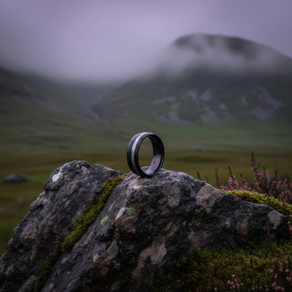 Black zirconium wedding band from Forge and Lumber, 8mm width, set on a rocky landscape.