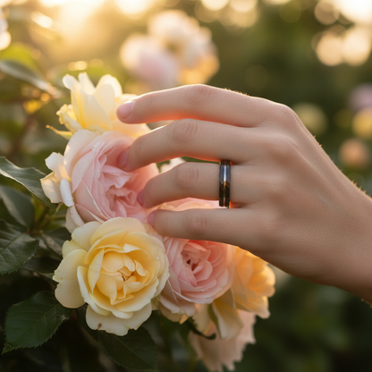 Delicate silver 4mm band ring from Forge and Lumber, shown on a hand among yellow and pink roses.
